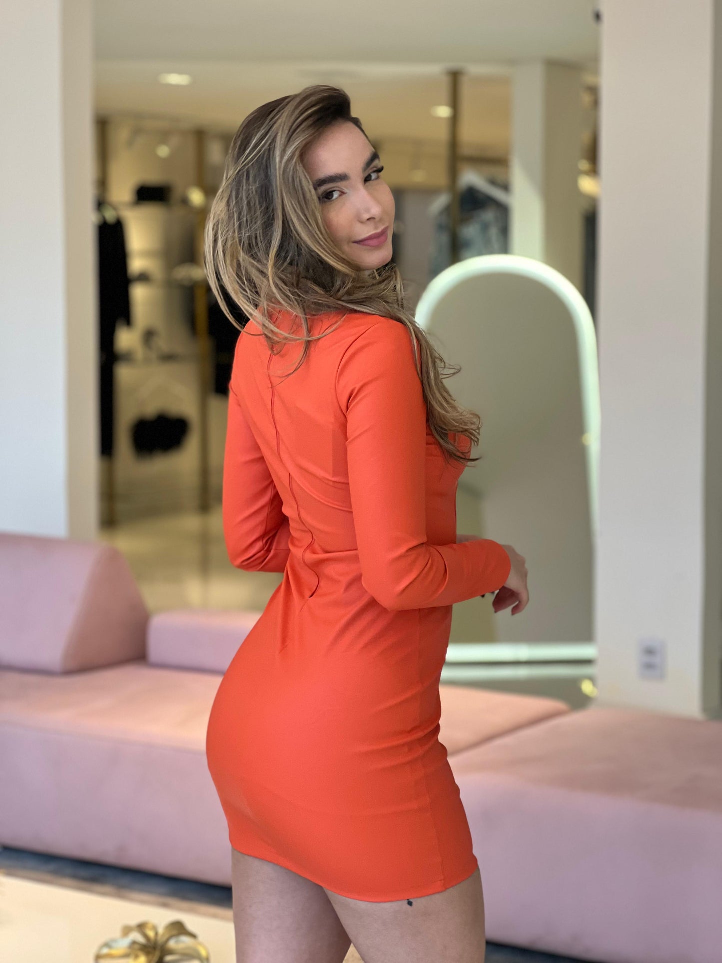 Vestido curto com manga longa da marca Lopz, em tom laranja, exibido na modelo em uma foto de conceito.